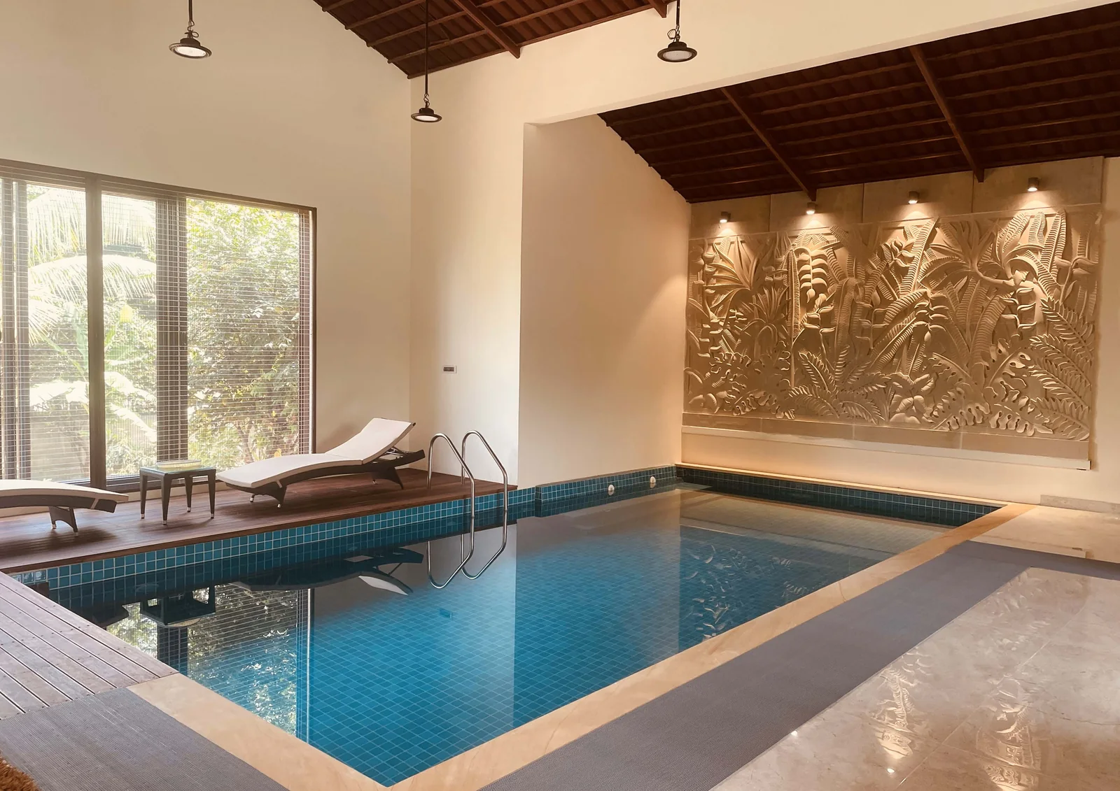 Indoor pool with teak deck and carved stone relief wall at Sanjeev Residence, Bangalore