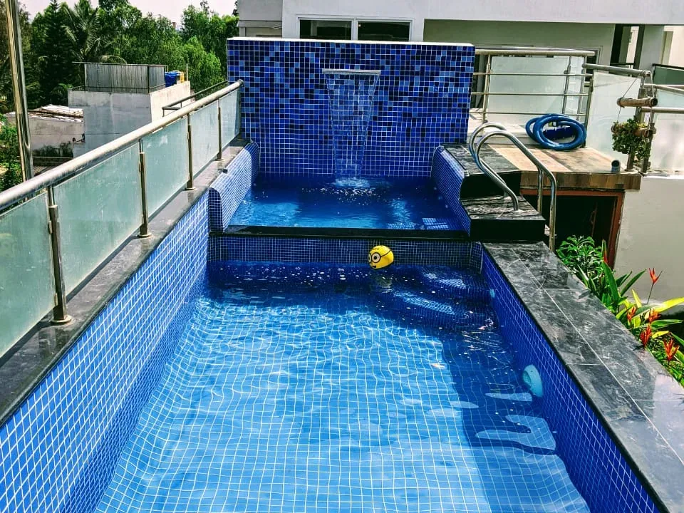 Rooftop pool with glass balustrade and mosaic waterfall wall at Rajeev Residence