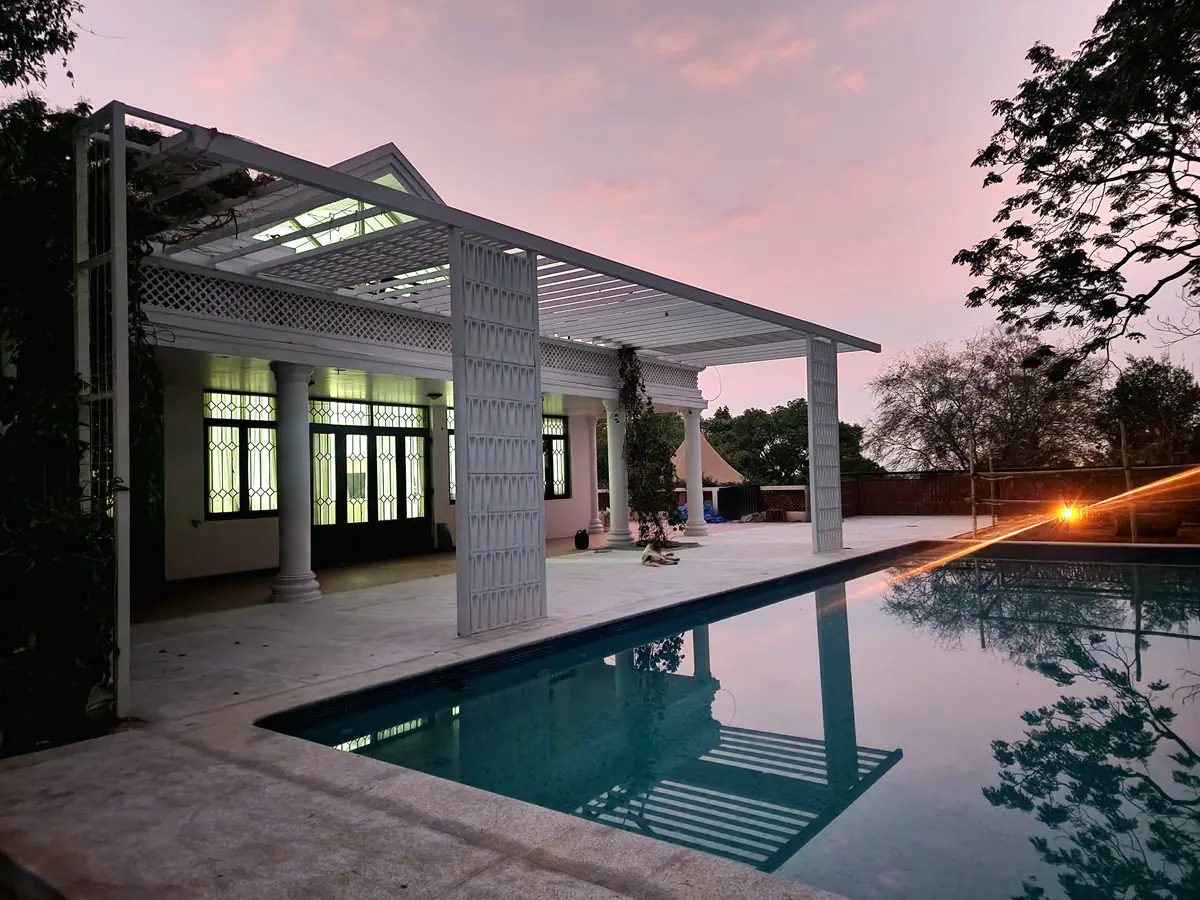 Lap pool reflecting a lit pergola at dusk at Raveen Residence, Bangalore